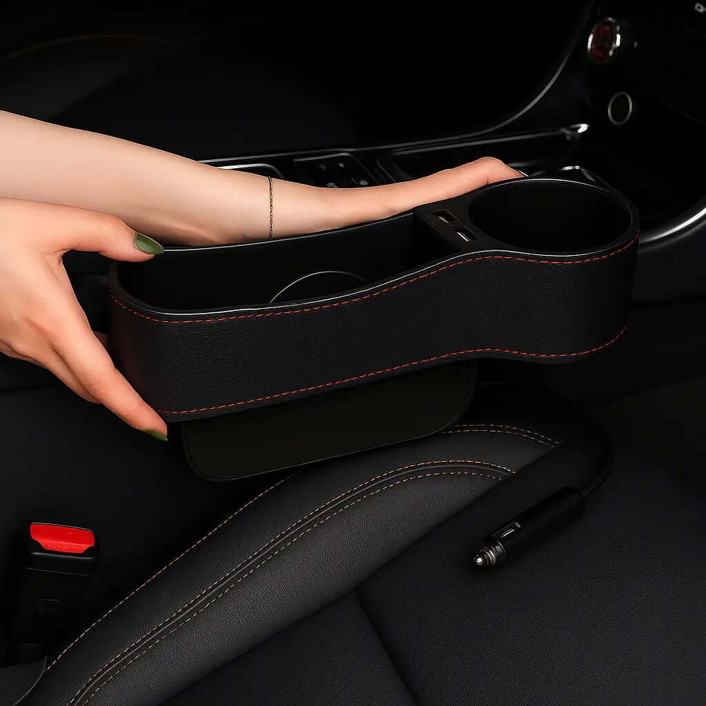 Black car seat gap filler with red stitching held by a hand inside a vehicle.